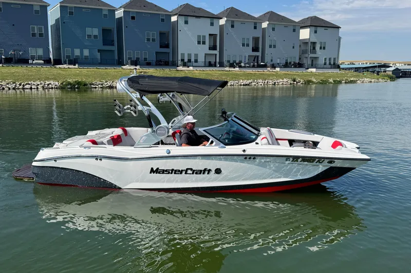 Slide: The Image of 2021 MasterCraft X22 boat on a calm lake near modern houses. - 1