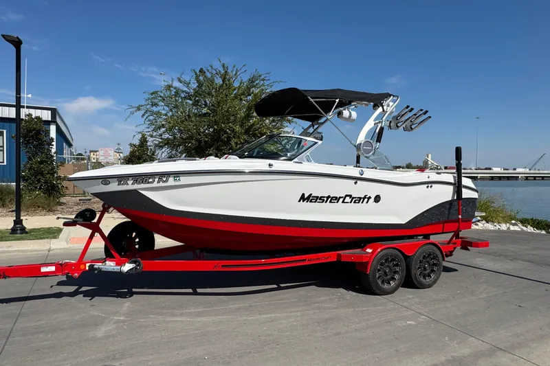 Slide: The Image of 2021 MasterCraft X22 boat on red trailer, parked near waterfront. - 6