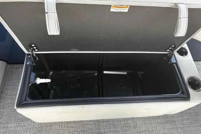 Slide: The Image of Open storage compartment on 2024 Barletta Cabrio 24CC boat, featuring cup holders and drainage. - 13