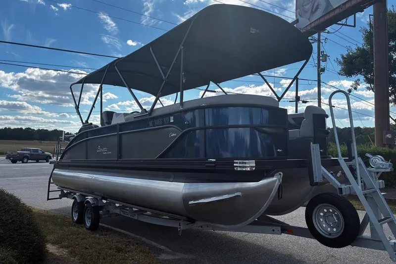 Slide: The Image of 2024 Barletta Cabrio 24CC pontoon boat with canopy on trailer, parked outdoors. - 2