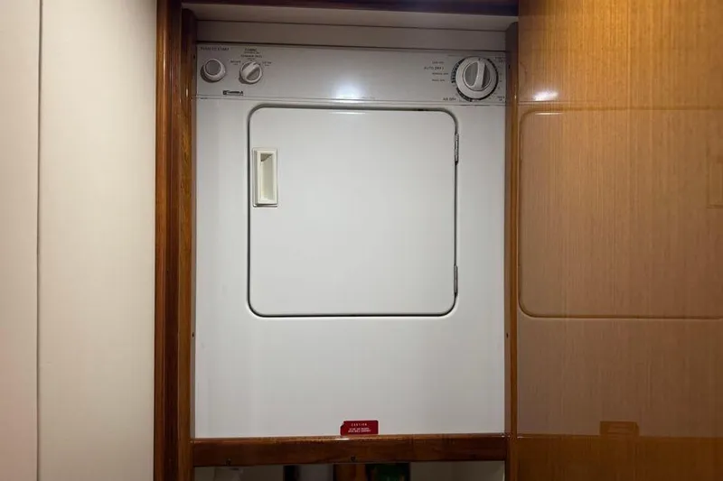 Slide: The Image of Laundry area inside 2002 Viking 61 Enclosed Bridge yacht, featuring a compact dryer. - 95