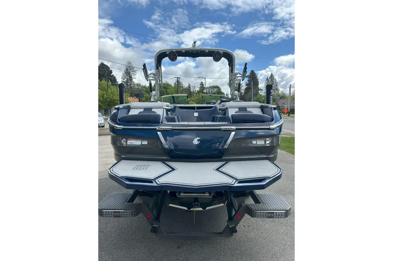 Slide: The Image of 2021 MasterCraft X24 boat, rear view, parked outdoors under a partly cloudy sky. - 2