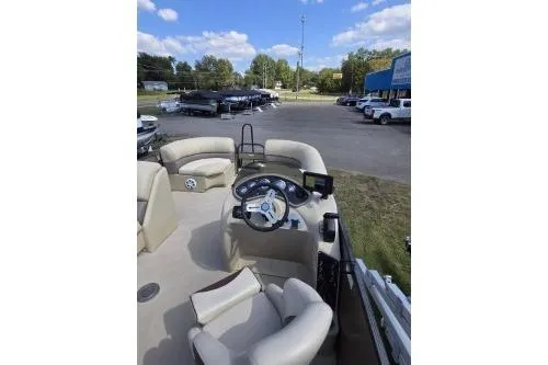 Slide: The Image of 2015 Manitou 20 Oasis Angler boat interior with steering wheel and seating, parked outdoors. - 10