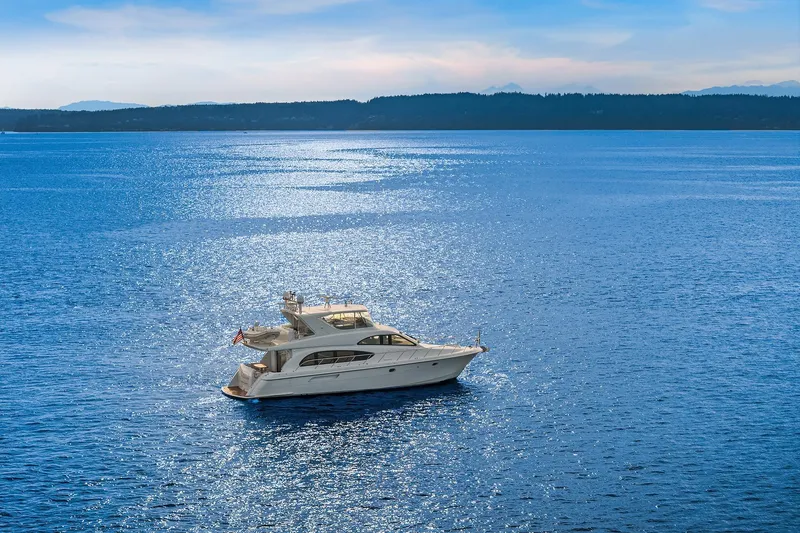 Slide: The Image of 2001 Hatteras 63 Cockpit Motor Yacht on serene blue water with lush green shoreline. - 34