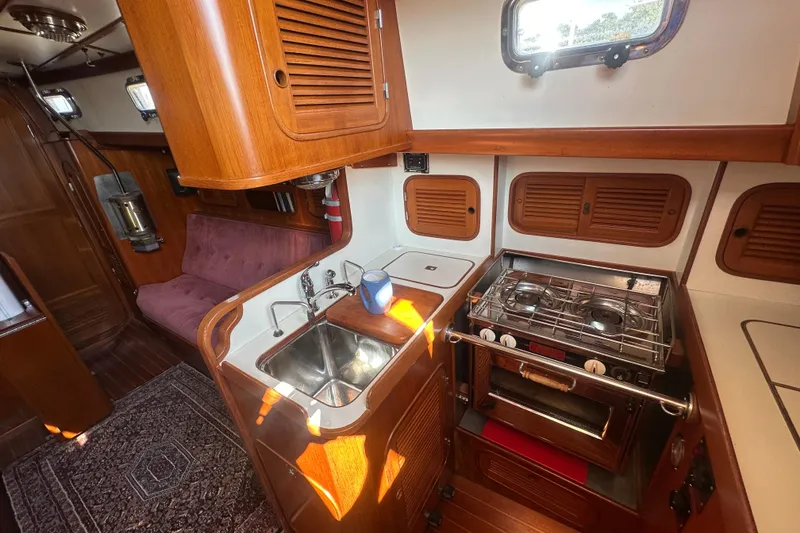 Slide: The Image of 1986 Mason 33 yacht interior with wooden cabinetry, compact kitchen, and cozy seating area. - 33