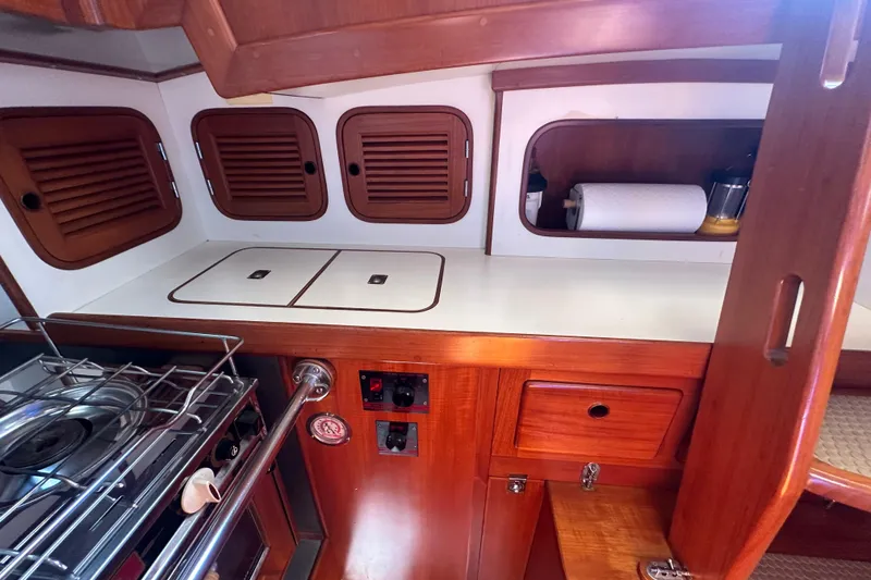 Slide: The Image of 1986 Mason 33 yacht kitchen with wooden cabinets, stove, and storage compartments. - 34