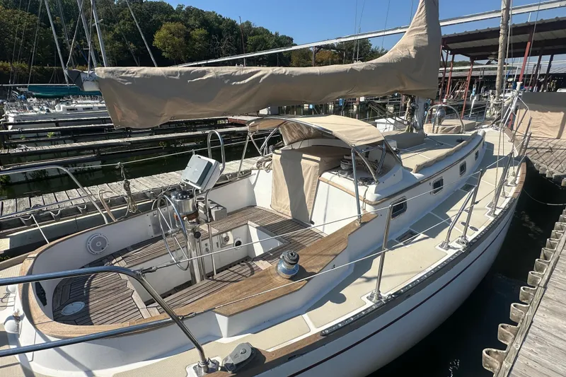 Slide: The Image of 1986 Mason 33 sailboat docked, featuring a spacious deck and beige sail cover. - 8