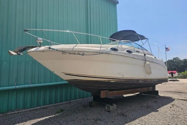 The Image of 2001 Sea Ray 260 Sundancer boat on dry dock, near green building, sunny day. - 0