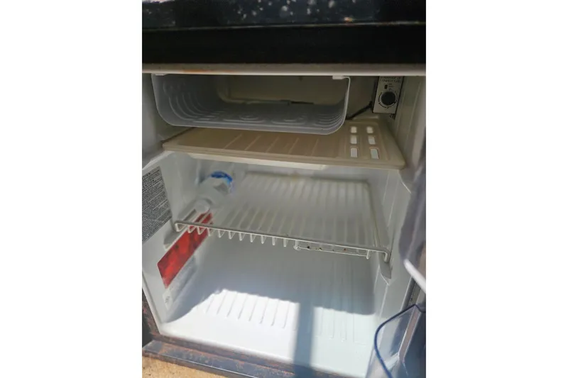Slide: The Image of Open mini fridge inside 2001 Sea Ray 260 Sundancer boat, showing empty shelves. - 23