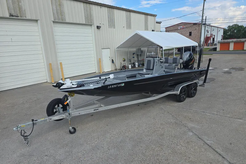 Slide: The Image of 2024 Xpress H22B Bay boat on trailer, parked outside industrial building. - 2