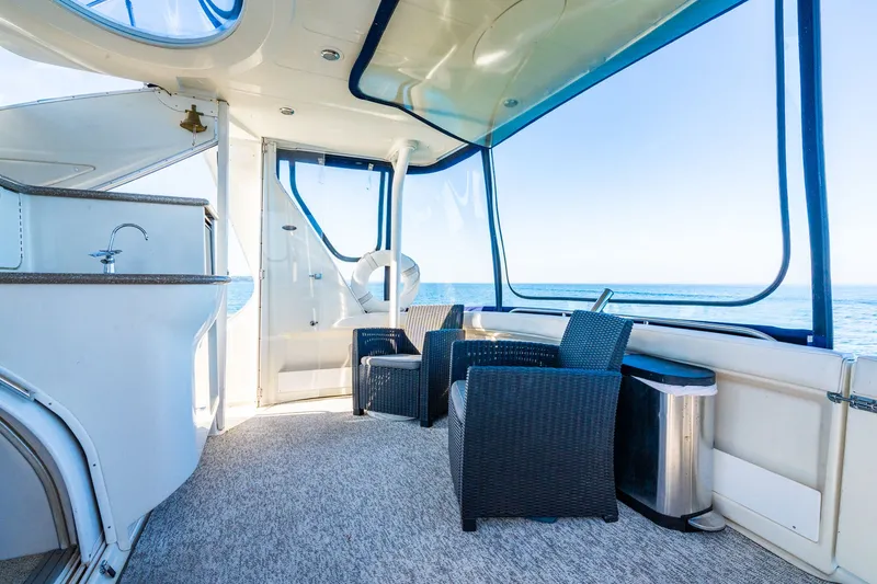 Slide: The Image of 1999 Maxum 4100 SCA Motor Yacht interior with ocean view, featuring wicker chairs and a kitchenette. - 26