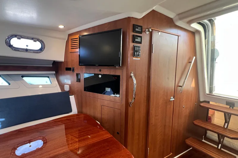 Slide: The Image of 2026 Pursuit OS 355 Offshore cabin interior with wood finish, TV, and stairs. - 19