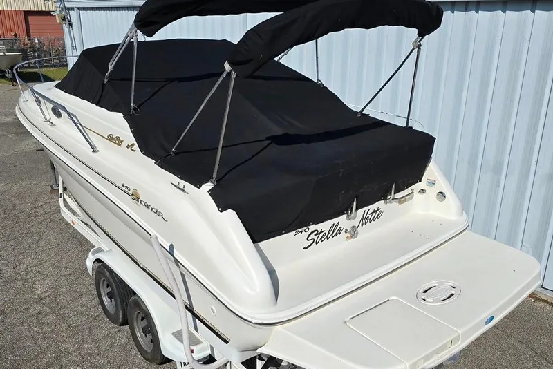 Slide: The Image of 1997 Sea Ray 240 Sundancer boat with black cover on trailer, parked near blue building. - 33