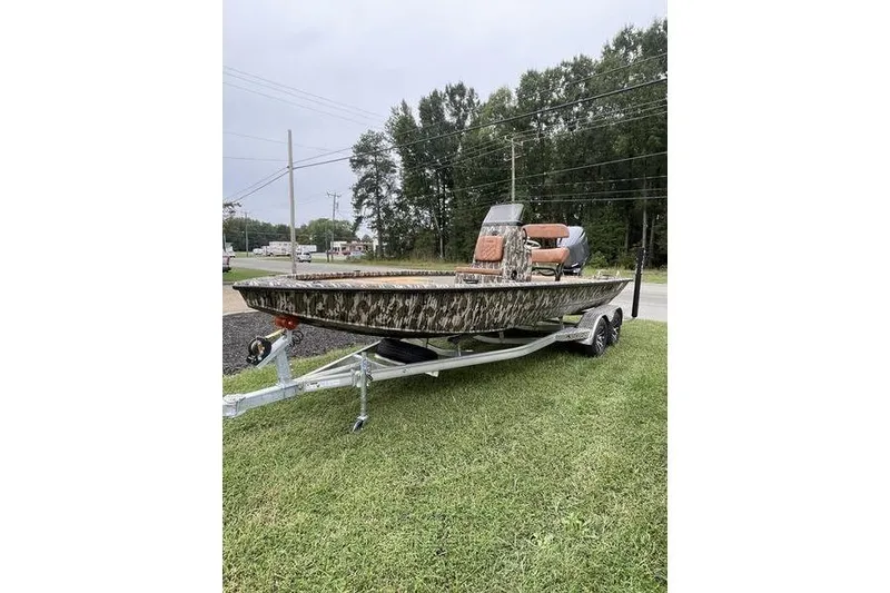 Slide: The Image of 2026 Avid 21 FSX boat with camouflage design on a trailer, parked on grass. - 0