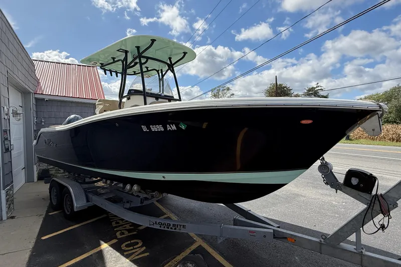 Slide: The Image of 2020 NauticStar 2602 Legacy boat on trailer, parked near building under blue sky. - 7