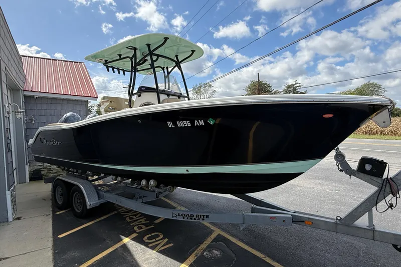 Slide: The Image of 2020 NauticStar 2602 Legacy boat on trailer, parked outdoors under a partly cloudy sky. - 8