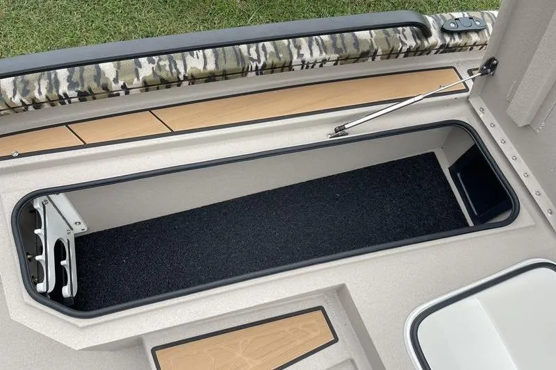 Slide: The Image of Avid 21 Fusion 2026 boat storage compartment with camo padding and carpeted interior. - 11