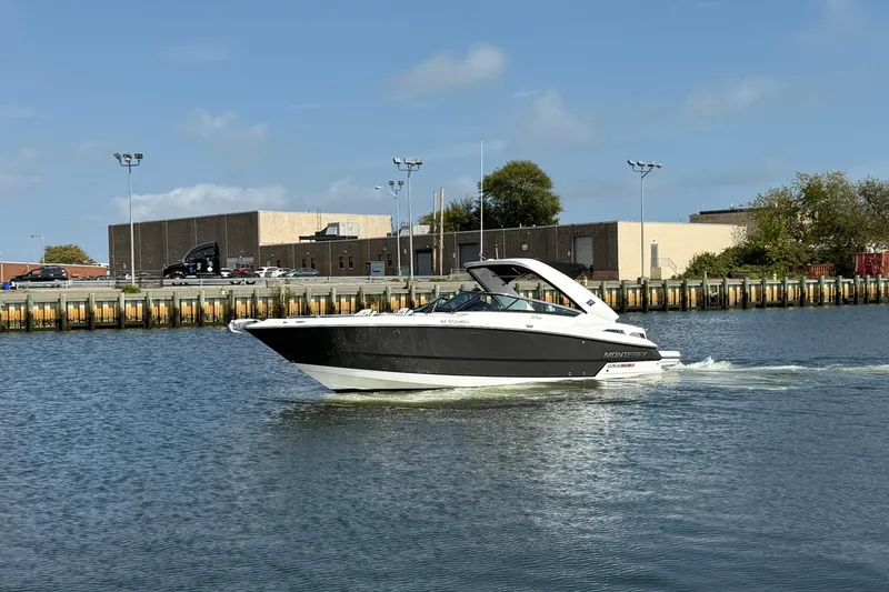 Slide: The Image of 2018 Monterey 328SS Super Sport boat cruising on a calm waterway near industrial buildings. - 3