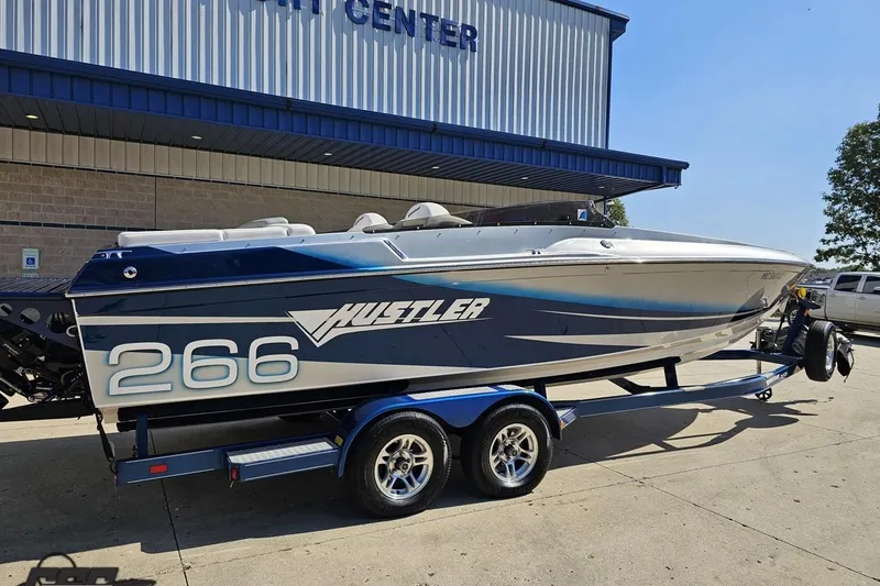 Slide: The Image of 2010 Hustler 266 Classic speedboat on trailer outside a yacht center. - 10