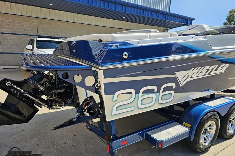 Slide: The Image of 2010 Hustler 266 Classic boat on trailer, blue and white design, parked outdoors. - 11