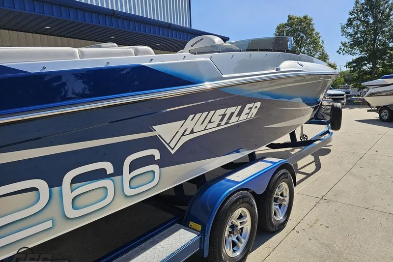 Slide: The Image of 2010 Hustler 266 Classic speedboat on trailer, blue and white design, parked outdoors. - 12
