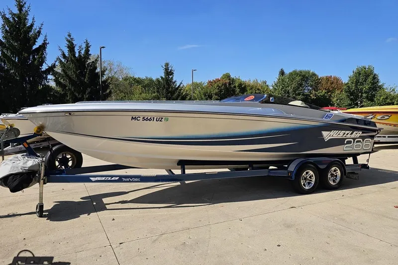 Slide: The Image of 2010 Hustler 266 Classic speedboat on trailer, parked outdoors with trees in background. - 18