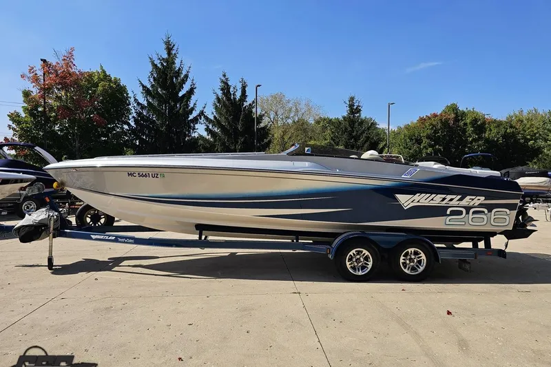 Slide: The Image of 2010 Hustler 266 Classic speedboat on trailer, parked outdoors with trees in background. - 19