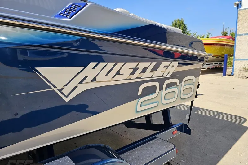 Slide: The Image of 2010 Hustler 266 Classic boat, blue and white design, parked outdoors. - 22