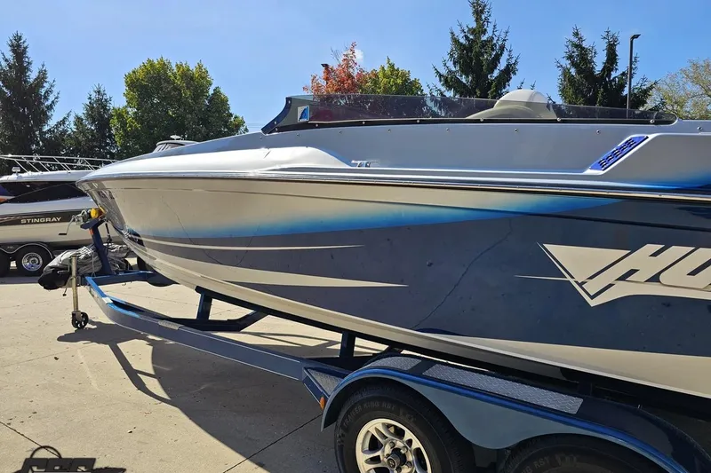 Slide: The Image of 2010 Hustler 266 Classic boat on trailer, parked outdoors with trees in background. - 24