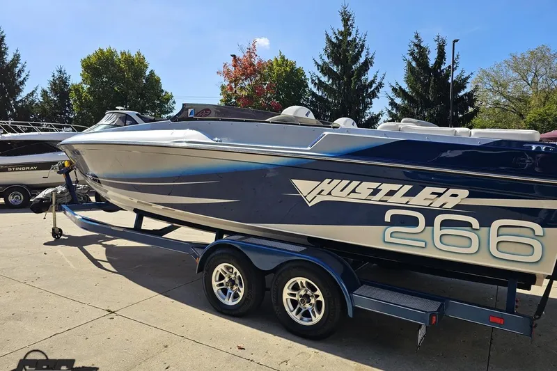 Slide: The Image of 2010 Hustler 266 Classic speedboat on trailer, parked outdoors with trees in background. - 25