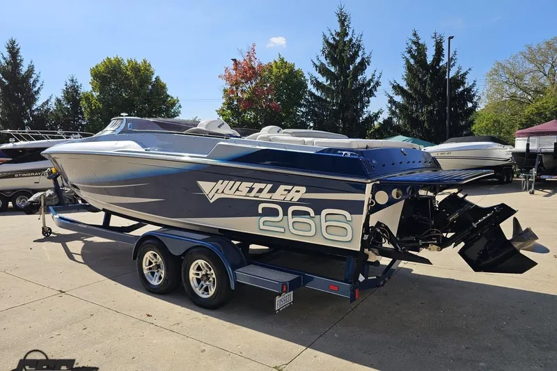 Slide: The Image of 2010 Hustler 266 Classic speedboat on trailer, parked outdoors with trees in background. - 26