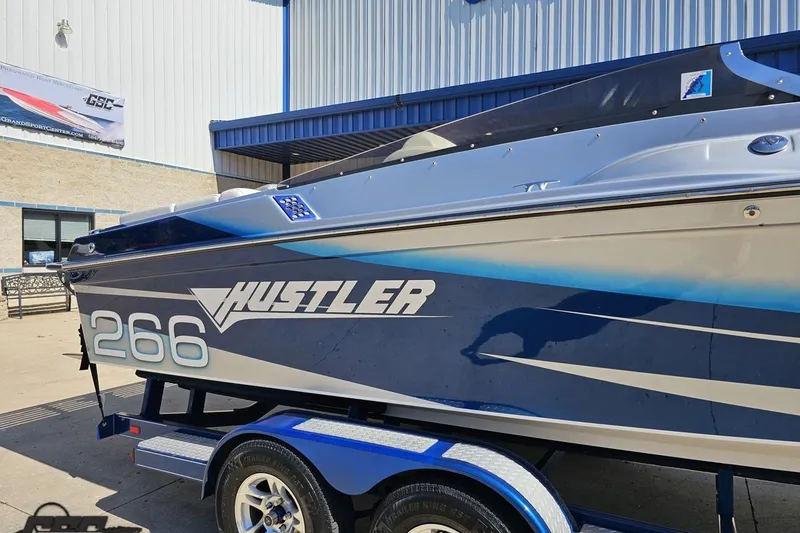 Slide: The Image of 2010 Hustler 266 Classic boat on trailer, blue and white design, parked outside building. - 6