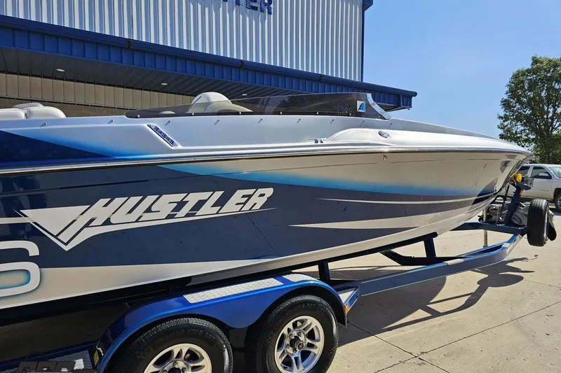 Slide: The Image of 2010 Hustler 266 Classic speedboat on trailer, parked outside a blue building. - 9