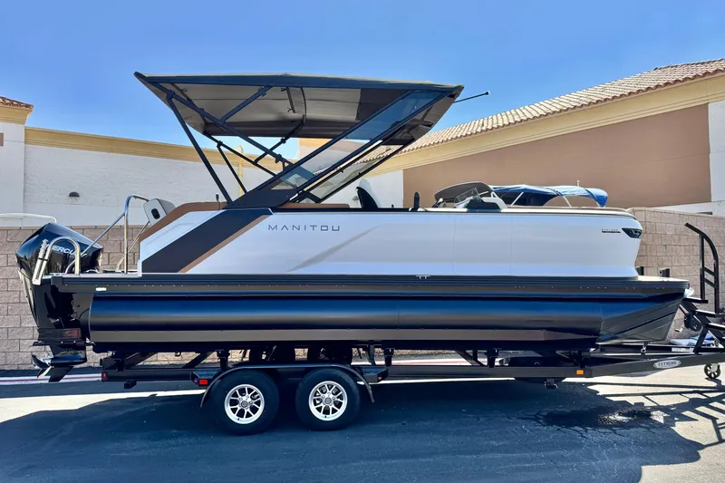 The Image of 2026 Manitou EXPLORE 22 pontoon boat on trailer, featuring sleek design and modern canopy. - 0