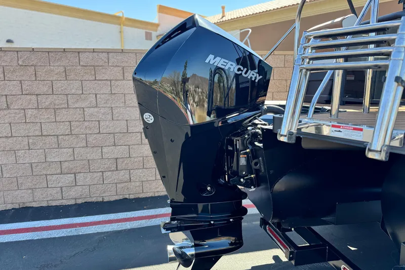 Slide: The Image of 2026 Manitou EXPLORE 22 with Mercury outboard motor, parked near a brick wall. - 7