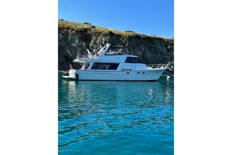 Slide: The Image of 2002 Bayliner 4788 Pilot House Motoryacht anchored in clear blue water near rocky cliffs. - 4