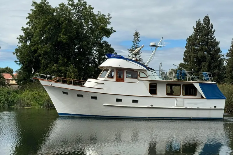 The Image of 1979 De Fever Pilot House boat on calm water, surrounded by lush greenery. - 0