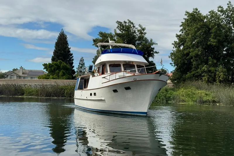 Slide: The Image of 1979 De Fever Pilot House yacht cruising on a serene waterway, surrounded by lush greenery. - 10