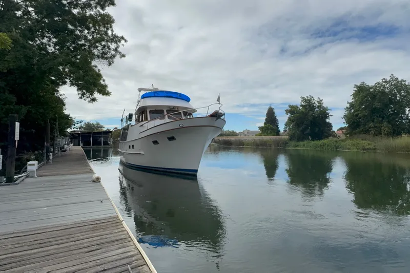 Slide: The Image of 1979 De Fever Pilot House yacht docked on a serene river with lush greenery. - 11