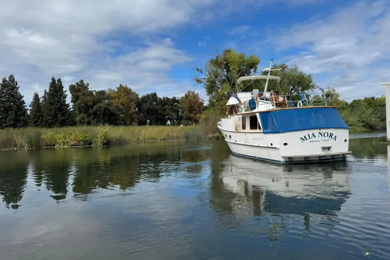 Slide: The Image of 1979 De Fever Pilot House boat "Mia Nora" on a serene river with lush greenery. - 3