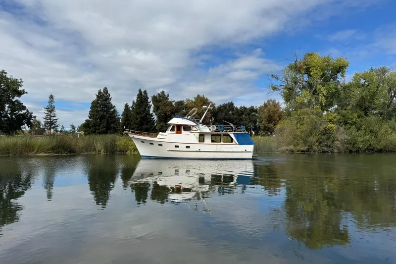Slide: The Image of 1979 De Fever Pilot House boat on calm water, surrounded by lush greenery and blue sky. - 4