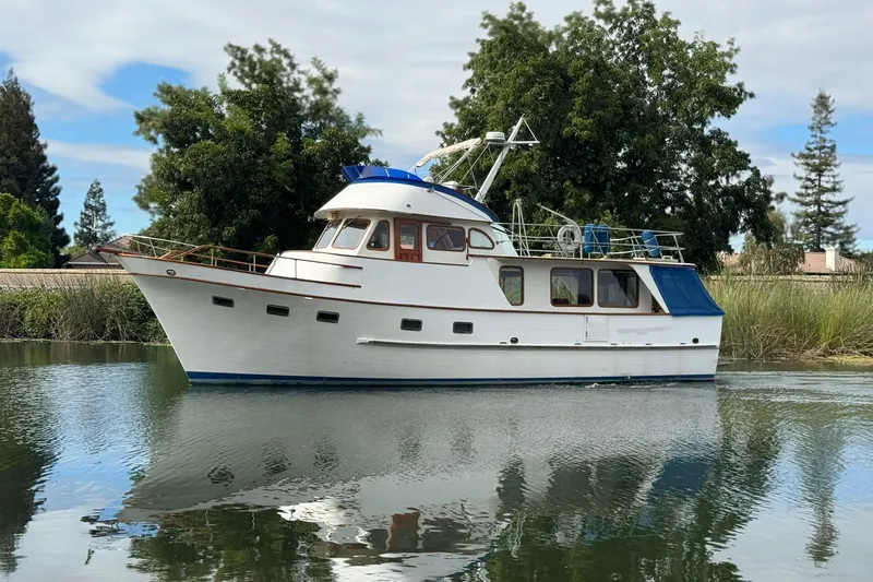 Slide: The Image of 1979 De Fever Pilot House yacht on calm water, surrounded by lush greenery. - 5