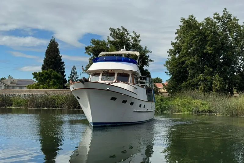 Slide: The Image of 1979 De Fever Pilot House yacht on calm water, surrounded by lush greenery. - 6