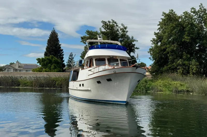 Slide: The Image of 1979 De Fever Pilot House boat on calm water, surrounded by lush greenery. - 8