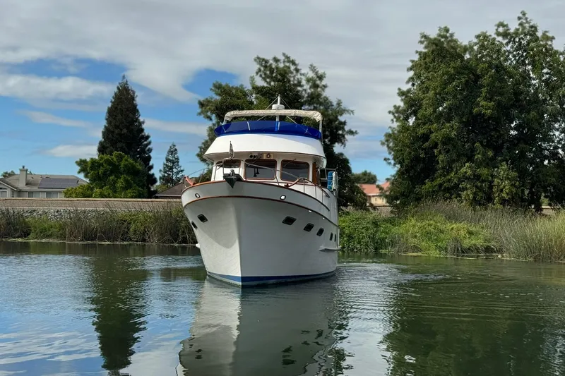 Slide: The Image of 1979 De Fever Pilot House boat on calm water, surrounded by lush greenery. - 9