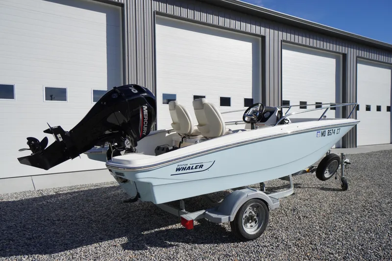 Slide: The Image of 2023 Boston Whaler 130 Super Sport boat on trailer, parked outside a garage. - 17