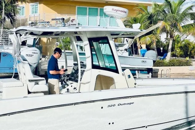 Slide: The Image of 2016 Boston Whaler 320 Outrage boat docked, with a person onboard, near a tropical setting. - 15