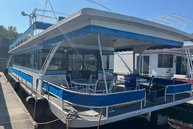 The Image of 1992 Jamestowner 16x72 houseboat docked, featuring blue accents and outdoor seating. - 0