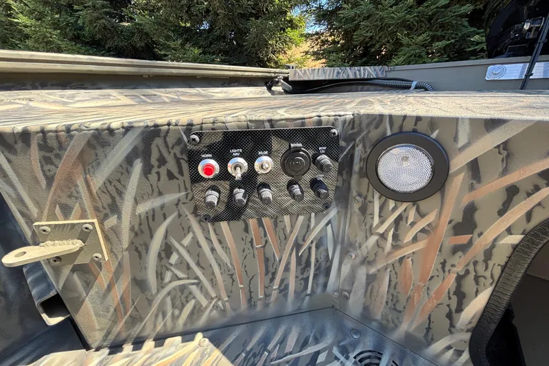 Slide: The Image of 2026 Tracker Grizzly 1654 T Sportsman boat control panel with camouflage design and switches. - 19