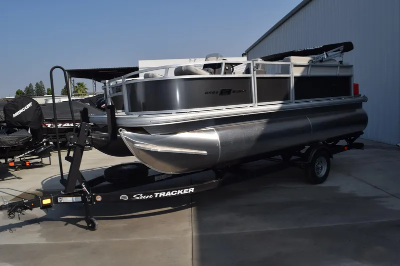 Slide: The Image of 2026 Sun Tracker Bass Buggy 16 XL Select pontoon boat on trailer, parked outdoors. - 2